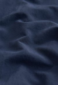 Tissu bleu foncé avec une texture douce et lisse et de légères plis créant un motif ondulé subtil à la surface.