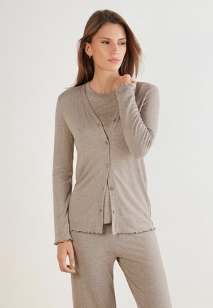 Cardigan beige clair et haut assorti, confectionnés en tissu doux et texturé avec une fermeture à boutons et des détails de manches en forme de vagues. Coupe décontractée.