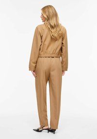 Veste courte marron avec taille élastique, assortie à un pantalon large de même couleur. Tissu lisse avec une finition mate et une texture subtile.