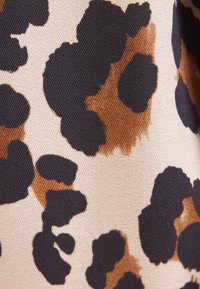 Gros plan sur un tissu avec des taches irrégulières d’imprimé léopard noir et brun sur un fond beige clair.
