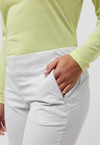 Lichtgroene langesleeve top gecombineerd met grijze outdoor broek met een ritszak en logodetail op de bovenbeen. Zachte, rekbare stof.