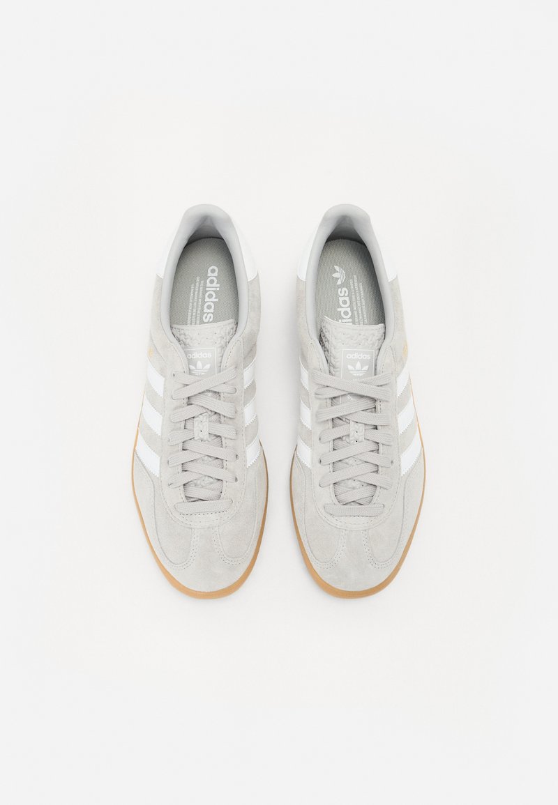 Zapatillas de ante gris claro con rayas blancas, diseño de cordones y suela de goma. Presenta logotipo en el talón y la lengüeta.