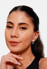 Orecchini a cerchio in argento con un design moderno a forma di U, caratterizzati da una finitura liscia e di dimensioni medie, indossati da una modella.