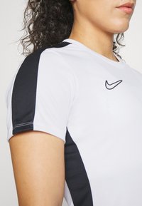 Maglietta atletica bianca con inserti in rete neri sulle spalle, caratterizzata da un piccolo logo Nike ricamato sul petto e da una scollatura a girocollo.