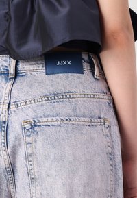 Svetlo prano denim jeans z modro oznako blagovne znamke na hrbtni strani. Ima ravne žepke in podrobnosti v rumenem šivanju.