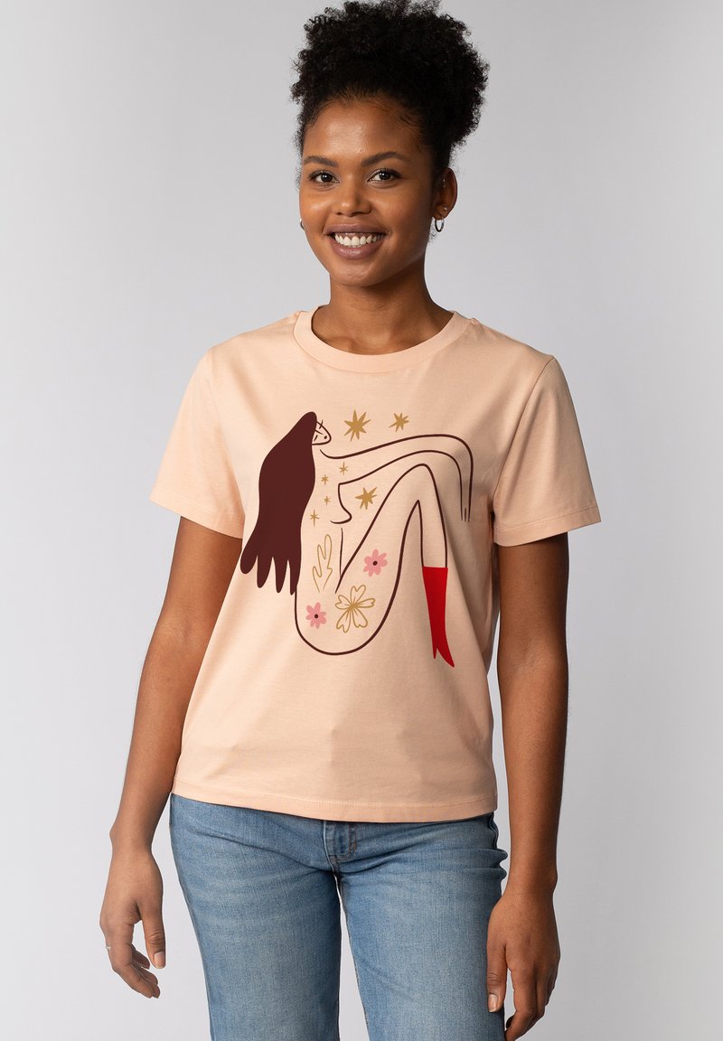 Pfirsichfarbene Baumwoll-T-Shirt mit Rundhalsausschnitt, das eine Grafik einer in Braun umrandeten Figur zeigt, die mit floralen Details und roten Akzenten geschmückt ist.