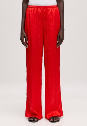 Red satin wide-leg trousers feature a textured, pleated design with an elastic waistband. Pairing well with flat sandals.