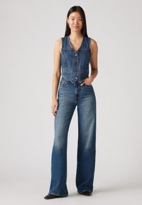 Denimvest med en tettsittende design, knappelukking foran og flettede detaljer. Kombinert med bredbente denimjeans i mellomblå vask.