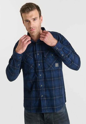 Camisa de cuadros azul con manga larga, dos bolsillos en el pecho, cierre frontal con botones, tejido texturizado y un pequeño parche de logo en el bolsillo izquierdo.