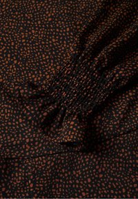 Schwarzer Stoff mit einem orangefarbenen, gepunkteten Muster; am Rand mit Raffung verziert. Weiche Textur mit fließendem Fall.