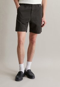 Donker khaki katoenen shorts met een elastische tailleband, zijzakken en een relaxte pasvorm. Gepaard met witte sokken en zwarte instappers.