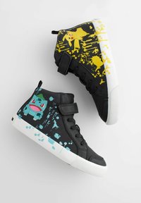 Zwarte hoge sneakers met een witte zool. De ene schoen heeft een gele Pikachu-afbeelding en een spetters ontwerp; de andere heeft een blauwe Bulbasaur-afbeelding.