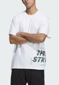 T-shirt bianca in cotone con maniche corte, caratterizzata da una grande stampa grafica grigia "THREE STRIPES" sul lato inferiore sinistro.