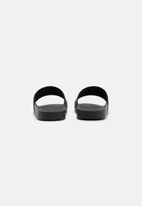 Sorte slippers i svart med glatte plastremmer og teksturert såle, med flat design og minimalistisk estetikk.