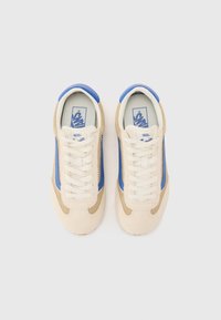 Beige semskede sneakers med blå side-striper, hvite snøringer, rund tå og teksturerte detaljer. Har Vans-logo på tungen.