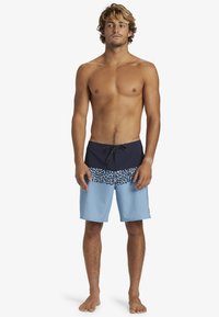 Shorts de bain avec une taille bleu marine, un motif texturé bleu et noir, et un tissu bleu clair uni. Conçus pour les activités aquatiques.
