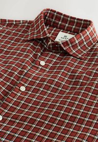 Chemise à carreaux rouges en coton, dotée d'un col classique, de boutons blancs et d'un motif à carreaux avec des accents blancs et noirs.
