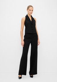 Haut sans manches noir avec des pois blancs, un col et des boutons sur le devant, assorti à des pantalons larges noirs et des talons noirs brillants.
