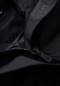 Interior de una chaqueta negra aislante con un forro suave, un cierre central con un tirador resistente y una textura sutil a lo largo de los bordes.