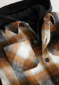 Flannel shirt with orange, brown, and white houndstooth pattern. Features black hood, button closures, and a soft, textured fabric.