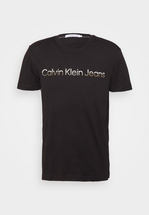 T-shirt noir à manches courtes et col rond avec le texte "Calvin Klein Jeans" en métal doré centré sur la poitrine.