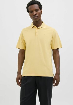 T-shirt polo jaune avec un col classique, des manches courtes et un logo discret sur la poitrine. Le matériau semble lisse avec une texture légère.