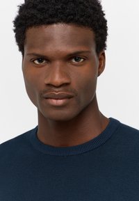 Rundhalsad tröja i mörk marin, stickad textur, kroppsnära design. Har ribbade muddar och halsringning, slät yta och inga synliga mönster.