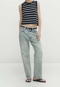 Prążkowany granatowy i biały bezrękawnik, krótki top dzianinowy, jasnoniebieskie luźne dżinsy, czarny pasek i czarne klapki na neutralnym tle.