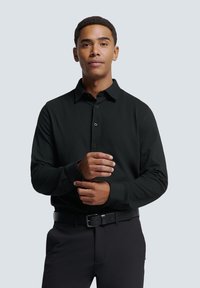 Zwart overhemd met lange mouwen en kraag, met een knoopsluiting aan de voorkant en een gladde textuur. Draag het met een zwarte broek en een riem.