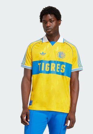 Kollane ja sinine jalgpalli särk lühikeste varrukatega, krae ja "TIGRES" trükiga rinna peal. Sisaldab Adidas logo ja struktureeritud mustrit.