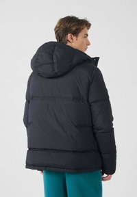 Zwarte gewatteerde jas met een trekkoordkap, voorzien van stevige secties en een eenvoudig ontwerp. De textuur lijkt zacht en geïsoleerd.