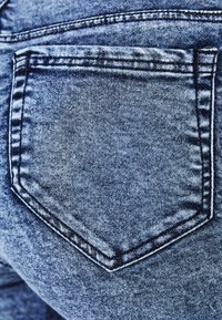 Kapsa z modrých džín s viditelným švem a texturovanou tkaninou v detailním záběru.