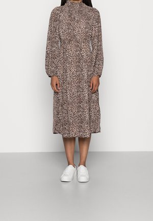 Robe à imprimé léopard avec de longues manches bouffantes, un col montant et une taille cintrée. Portée avec des baskets blanches pour un style décontracté.