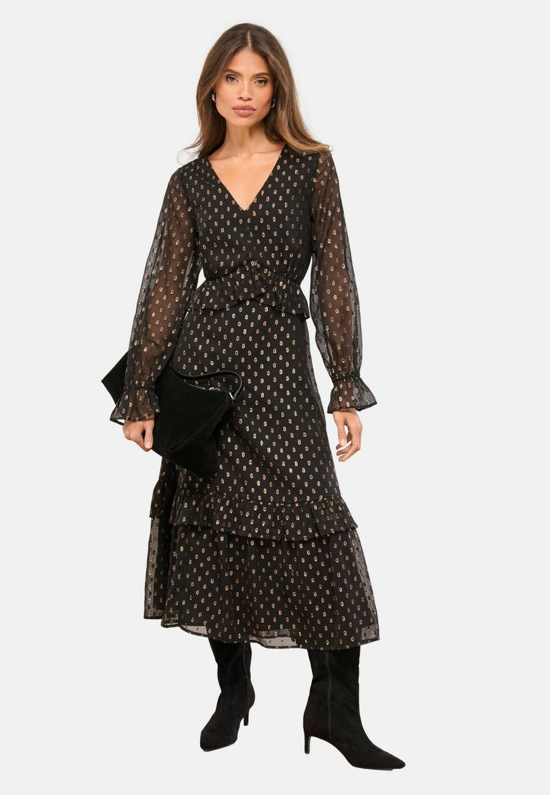 Rochie neagră cu mâneci lungi, decolteu în V, tiv cu volane și modele aurii. Asortată cu o geantă neagră și cizme negre până la genunchi.