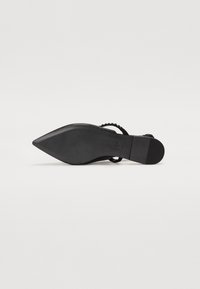 Chaussure noire à talon haut avec un bout pointu, semelle texturée et un design de bride tressée. Fini lisse qui complète un style minimaliste.