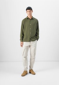 Olive green button-up shirt with a textured fabric, cream cargo pants with side pockets, and tan sneakers with a smooth finish.