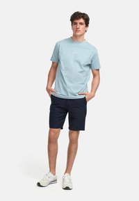 T-shirt in cotone azzurro chiaro con maniche corte e scollatura rotonda, abbinato a pantaloni corti navy. Indossato con scarpe da ginnastica bianche e beige.