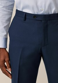 Pantalones de vestir en color marino con acabado texturizado, que presentan un cierre de un botón, presillas para cinturón y un diseño de frente plano.