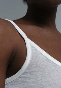 White cotton tank top featuring thin straps and a ribbed neckline, showing soft, breathable fabric texture against darker skin tone.