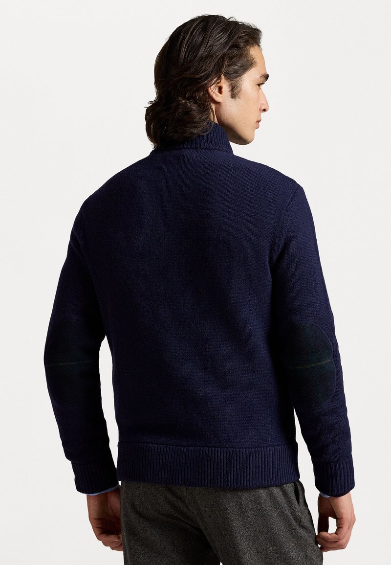 Navy wool sweater with a high collar, ribbed hem and cuffs, featuring green plaid elbow patches for added detail.