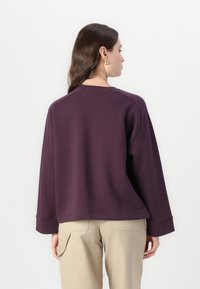 Felpa viola scuro con una vestibilità comoda, spalle scese e maniche ampie. Presenta un collo tondo e dettagli di cucitura sottili.