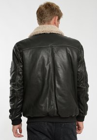 Svart läderjacka med en beige fårskinnskräm, ribbad nederkant och ärmslut samt synlig sömnad på baksidan.