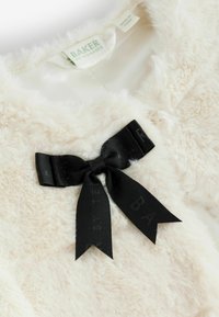 Baltas dirbtinis pūkuotas drabužis su šilkine vidine pamušalu, puoštas juodu satino kaspinu su iškaltu tekstu, pasižymintis minkštu, tekstūruotu dizainu.