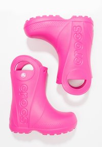 Jasnoróżowe gumowe kalosze z teksturowaną powierzchnią, okrągłymi uchwytami i wypukłym logo "crocs" po bokach.