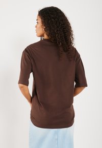T-shirt oversized marron à manches courtes et col rond. Texture douce, ourlet droit et design minimaliste.