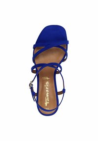 Modra nobučna sandal z ravnim podplatom, križanimi trakovi in zaponko okrog gležnja. Notranji sole je svetlo rjav in vsebuje logotip.