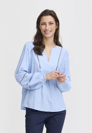Blusa azzurra chiara con scollo a V e maniche a sbuffo, con tagli decorativi lungo il décolleté e i bordi delle maniche. Tessuto liscio e tessuto.