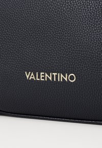 Černá strukturovaná kožená kabelka s výrazným zlatým logem "Valentino". Materiál má jemnou reliéfní strukturu s hladkým povrchem.
