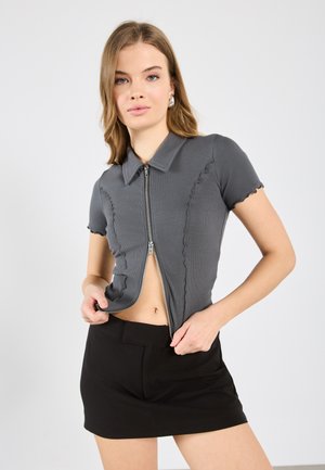 Graues, geripptes T-Shirt mit kurzen Ärmeln, einem Reißverschluss und gewellten Kanten, kombiniert mit einem schwarzen Minirock. Schlichtes Design und figurbetonte Silhouette.