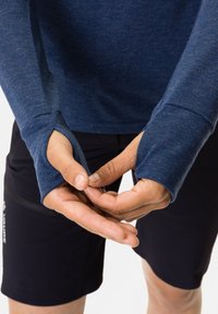 Maglietta a maniche lunghe di colore blu melange con aperture per il pollice nei polsini, abbinata a pantaloni shorts neri. Il materiale sembra morbido e dalla consistenza particolare. Mani che mostrano l'addattamento dei polsini.